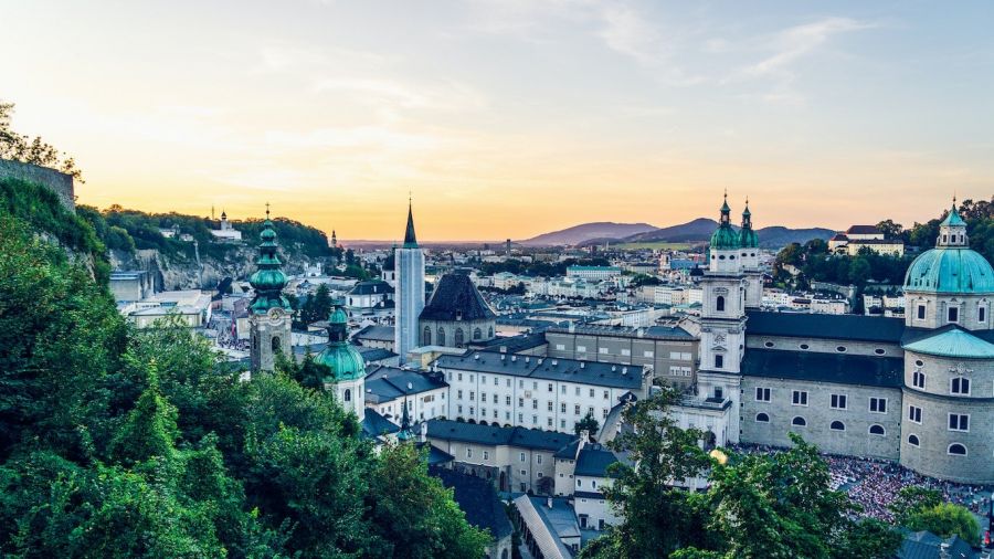 A beautiful sunset over a cityscape showcasing historic architecture with domed roofs and church steeples. On the left, a lush hillside is framed against the warm, colorful sky filled with orange and pink hues as dusk approaches. The urban scene reflects tranquility and timeless beauty at this unique wedding destination perfect for creating memorable ceremonies in Dubai or Abu Dhabi.