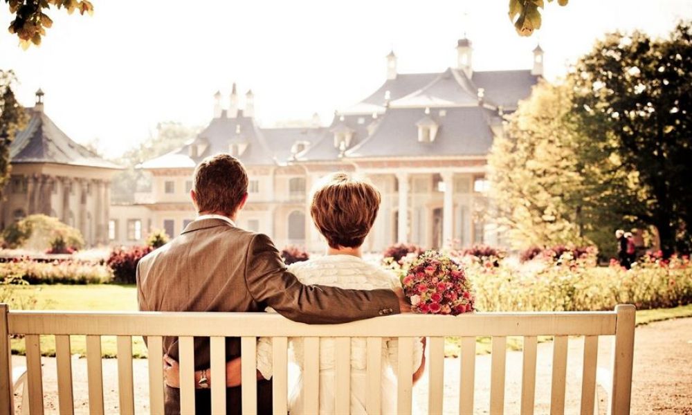 What Type Of Wedding Certificate Will You Get If You Can T Get Married In Dubai And Opt To Get Married Online | Online Marriage Dubai - What Type Of Wedding Certificate Will You Get If You Can’t Get Married In Dubai And Opt To Get Married Online? | Regardless Of The Current Situation Of The World, Dubai Is Not An Ideal Place To Get Married. It’s Because Of Its Long Wedding Procedure That Sometimes Can Easily Take Months. But There Are Also Many Situations When You Need To Get Married In The Least Possible Time. So, In That Situation Getting Married In Dubai Is Certainly Not Advisable In General Cases. If You Choose To Get Married Online In That Situation, Have You Ever Wondered About The Getting Married Online Process And What Type Of Wedding Certificate You’ll Get? We Have Compiled This Article For You That Will Provide You With The Answer To This Question. So, Keep On Reading, So That You Can Go For Your Online Wedding With Peace Of Mind. A couple shares a romantic moment on a wooden bench in a picturesque garden. The groom wears a suit while the bride is dressed in white with a vibrant bouquet. They admire a large, charming building surrounded by lush trees and colorful flowers.