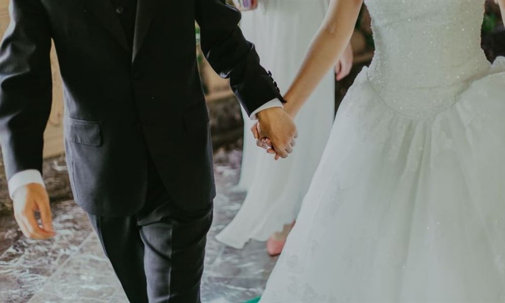 Pexels Jeremy Wong 1043902 1 | Decoding The Step-By-Step Procedure On How To Get Married In Abu Dhabi | In This Article We Decode The Step By Step Procedure On How To Get Married In Abu Dhabi. The image shows a happy couple on their wedding day walking hand in hand. The groom is in a classic black suit while the bride wears an elegant white gown with intricate details. They are captured joyfully mid-step against a backdrop of marble flooring and soft lighting that creates an intimate atmosphere celebrating their love on this special occasion.
