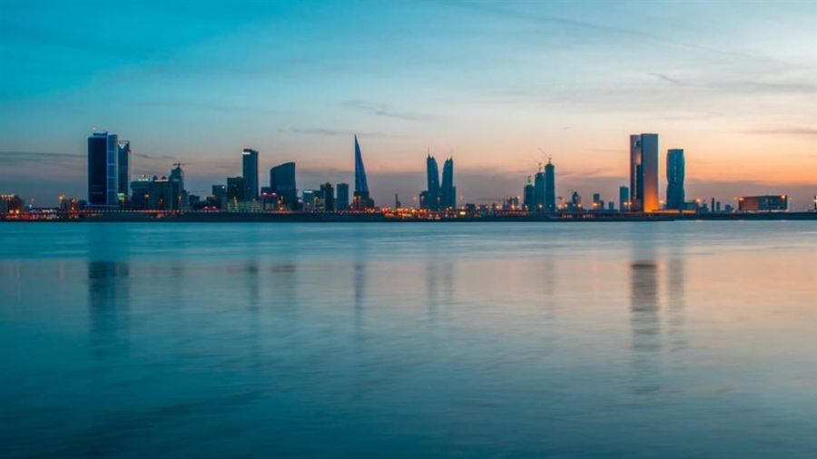 A relaxing image of Dubai's skyline at dusk viewed over calm water. The modern skyscrapers reflect beautifully on the water's surface while vibrant blue and orange hues fill the sky. A few cranes hint at construction progress, creating a dynamic atmosphere of urban life and natural beauty.