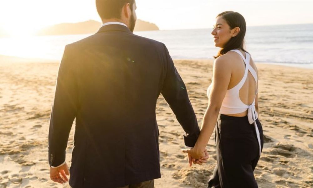 wedding packages in seychelles for dubai residents | Wedding packages in Seychelles for Dubai residents | If you still contemplating between a wedding in Seychelles from Dubai; allow us to help you make this fine decision; you wont regret it!</p> A couple walks hand in hand on a sandy beach during sunset. The man wears a dark suit while the woman has on a white top with black pants. The warm glow from the sun creates a romantic atmosphere as waves gently lap against the shore. The scene captures their joyful moments together surrounded by nature's beauty, showcasing calmness and happiness under a clear sky.