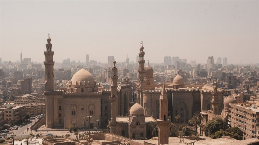 A warm panoramic view of Dubai showcasing a mix of historic buildings and modern skyscrapers under soft sunlight. The foreground features impressive Islamic architecture with tall minarets and large domes. The expansive skyline captures the vibrant spirit of the bustling city, making it ideal for celebrating love through weddings, ceremonies, and memorable moments.