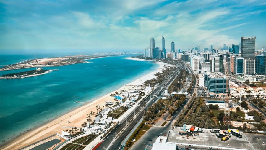 The image captures a breathtaking aerial view of Abu Dhabi showcasing modern skyscrapers against the turquoise Arabian Gulf. The beautiful coastline is lined with sandy beaches bordered by clear blue waters and vibrant palm trees. This enchanting scene perfectly blends natural beauty with urban setting, reflecting what makes Abu Dhabi unique as a wedding destination. Perfect for couples looking to get married surrounded by stunning landscapes and contemporary architecture.