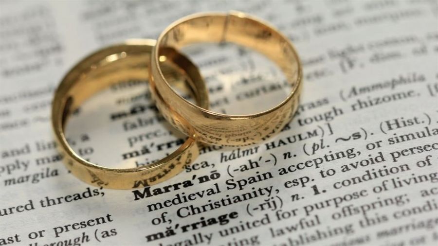 Two elegant gold wedding rings overlap on an open dictionary page showing the word “marriage.” The rings shine beautifully against a softly blurred background filled with text. This image represents commitment and love, capturing the essence of marriage in a charming way. The simple design of the rings complements their meaning, making it a delightful symbol of unity and celebration for weddings in Dubai.