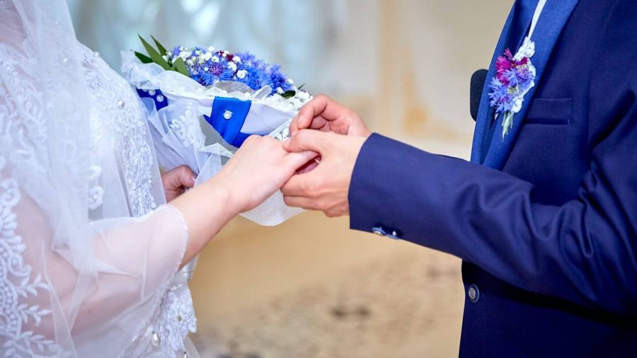 A lovely bride and groom share a tender moment as they exchange rings at their wedding ceremony. The bride wearing a delicate white dress holds a beautiful bouquet while the groom in a dark suit smiles lovingly. This image captures an intimate celebration filled with joy and warmth surrounded by elegant decor that enhances the romance of their special day in Dubai's magical atmosphere.