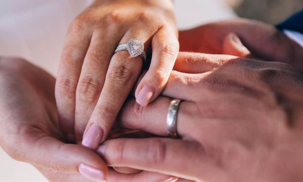 A close-up view of two hands exchanging rings symbolizes unity and commitment. One hand features an elegant engagement ring adorned with a sparkling diamond while the other hand, positioned below, wears a simple wedding band. The blurred background focuses attention on this meaningful moment. This image captures the essence of love and devotion during marriage ceremonies or proposals, encouraging couples to celebrate their special day together.