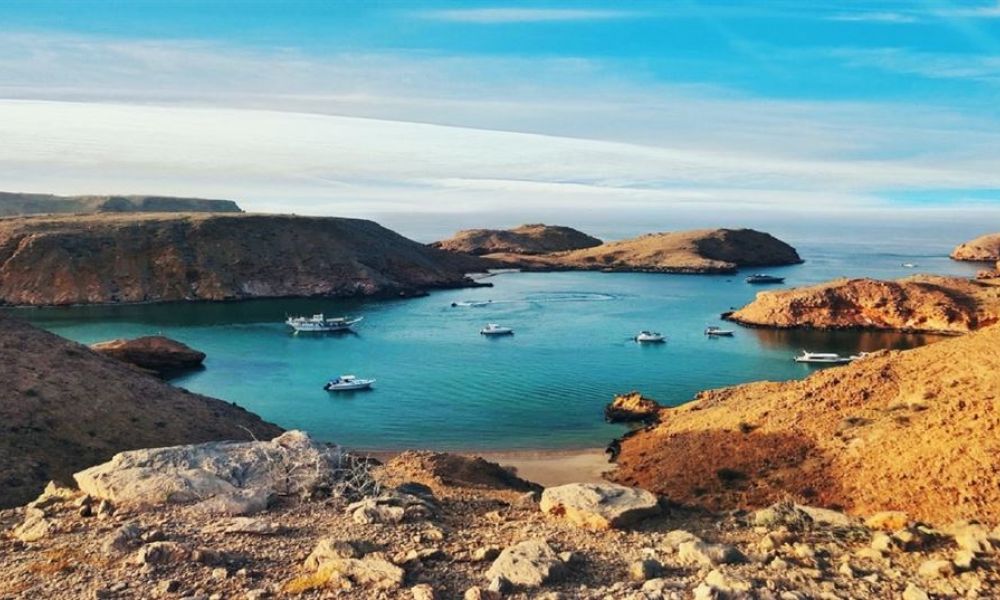 A picturesque coastal landscape shows rocky islands surrounded by calm turquoise waters. Small boats float gently in the tranquil bay while rugged terrain and scattered rocks add beauty to this serene scene. The sky above features soft clouds creating a peaceful atmosphere perfect for weddings or celebrations.