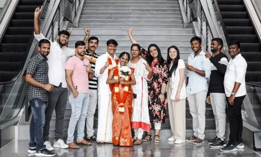 5 3Cbefded | Free Visa For Indian Couples: Host Your Destination Weddings In Abu Dhabi 2024 | The United Arab Emirates Now Offers Special Visa Support For Indians Planning To Host Destination Weddings In This Glamorous City. Abu Dhabi'S New Visa Program Is A Key Part Of Its Plan To Double Tourist Numbers And Significantly Boost The Tourism Industry'S Contribution To The Economy By 2030. Image of a smiling couple dressed in traditional attire standing at the center of a lively crowd on an escalator as friends cheer them on. The setting is bright and spacious with modern designs surrounding them.