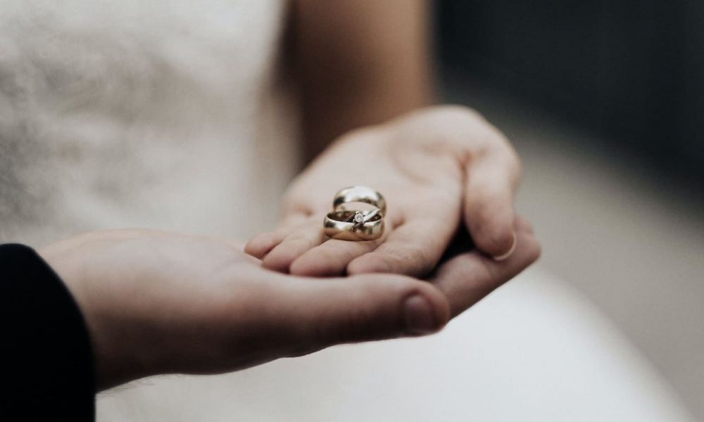 A lovely close-up image of two hands gently holding each other. One hand cradles two sparkling gold wedding rings resting softly in its palm. The background is blurred to emphasize the warmth and unity represented by the rings and hands. This image evokes feelings of love, commitment, and intimacy associated with weddings or engagements in Dubai.