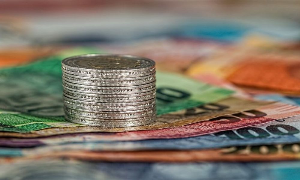An image showing shiny silver coins stacked in the center surrounded by colorful banknotes like green blue orange and purple placed beautifully suggests finance themes while focusing on their textures and designs.