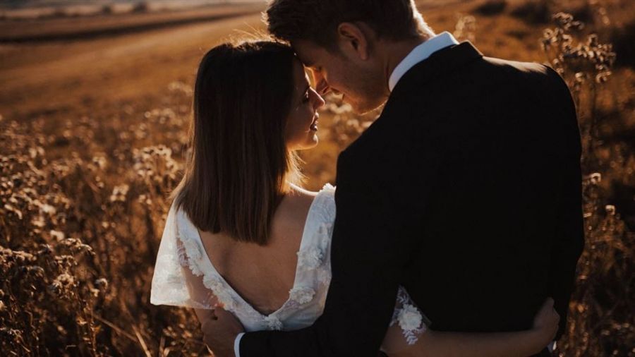 A couple shares a peaceful moment in a sunlit field during their wedding ceremony. The woman feels lovely in her white lace dress, while the man wears a dark suit. They are surrounded by gentle wildflowers, creating a romantic atmosphere filled with warmth and love. This image captures the essence of love and togetherness as they enjoy each other's company during this unforgettable day in beautiful Dubai.