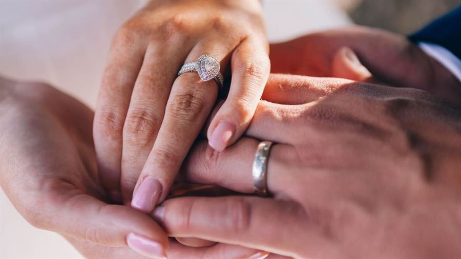 A close-up view of two hands exchanging rings symbolizes unity and commitment. One hand features an elegant engagement ring adorned with a sparkling diamond while the other hand, positioned below, wears a simple wedding band. The blurred background focuses attention on this meaningful moment. This image captures the essence of love and devotion during marriage ceremonies or proposals, encouraging couples to celebrate their special day together.