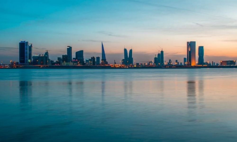 A relaxing image of Dubai's skyline at dusk viewed over calm water. The modern skyscrapers reflect beautifully on the water's surface while vibrant blue and orange hues fill the sky. A few cranes hint at construction progress, creating a dynamic atmosphere of urban life and natural beauty.