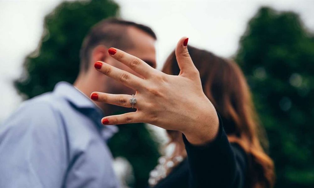 how to get married in dubai for foreigners 1d2d9859 | How to get married in Dubai for foreigners | A lot of foreigners or expats in Dubai are used to having to prepare a plethora of documents just to be able to live legally in the city. This is significant especially for couples who are looking to settle down in Dubai as paperwork for marriage can be finalized up to a year. The image shows a happy couple outdoors with smiles as they celebrate an engagement moment. The woman has her hand raised displaying a sparkling engagement ring while wearing bright red nail polish. The background features soft green foliage creating a romantic atmosphere. Both appear joyful, capturing an intimate celebration together which signifies their commitment.