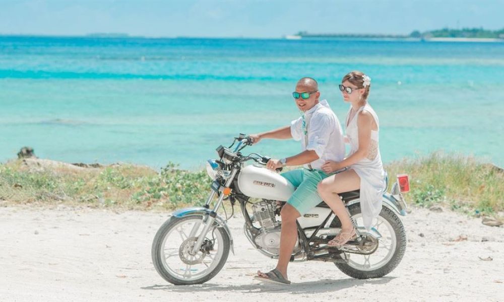 seychelles wedding packages for uae expats 24c84717 | Why are Seychelles wedding packages so popular amongst UAE Expats | Are you planning on getting married in Seychelles. If so; you have stumbled upon the right place. A happy couple rides a motorcycle along a beautiful beachfront in Dubai. They wear sunglasses and summery clothes, with turquoise ocean waters in the background under a bright blue sky. The sandy path beside them has scattered rocks and sparse plants, creating a peaceful atmosphere that speaks of adventure and relaxation.