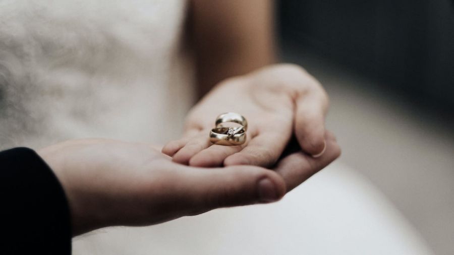 A lovely close-up image of two hands gently holding each other. One hand cradles two sparkling gold wedding rings resting softly in its palm. The background is blurred to emphasize the warmth and unity represented by the rings and hands. This image evokes feelings of love, commitment, and intimacy associated with weddings or engagements in Dubai.
