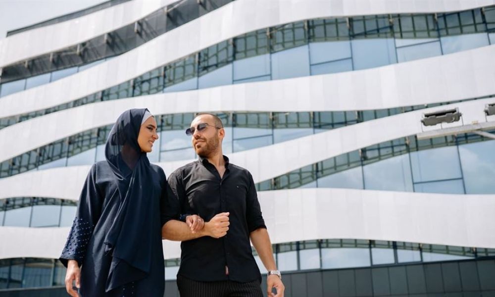 marriage procedure for foreigners in saudi arabia 470f4293 | Procedure for Foreigners Marriage in Saudi Arabia! | This article will inform you of all the necessary requirements to get married in Saudi Arabia. Moreover, it also contains very valuable information about the alternatives to get married more easily in the least possible time. Keep on reading to find out everything that you need to know about foreigners marriage in Saudi Arabia. So, Let’s jump into it. A couple stands happily together in front of a modern, wavy architectural building. The woman wears a dark blue hijab and matching abaya while the man is dressed casually in black with sunglasses. They are smiling at each other with joy as they embrace, surrounded by bright daylight and glass panels reflecting the sky behind them.