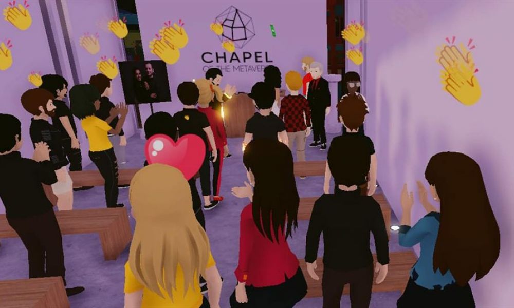 The image shows avatars celebrating a wedding ceremony inside a vibrant virtual chapel. With purple walls and wooden benches, guests are engaged at a podium where an avatar is presenting. Clapping hands and hearts float above them, demonstrating lively participation. The word CHAPEL is featured prominently on the wall, indicating this unique gathering space designed for joyous virtual celebrations like weddings.