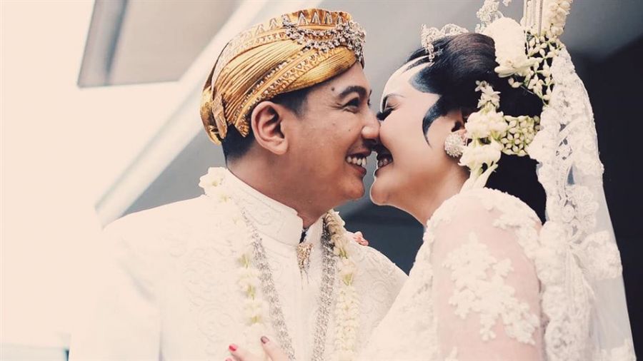 A joyful couple dressed in traditional wedding attire shares a loving moment on their special day surrounded by symbols of celebration and unity.