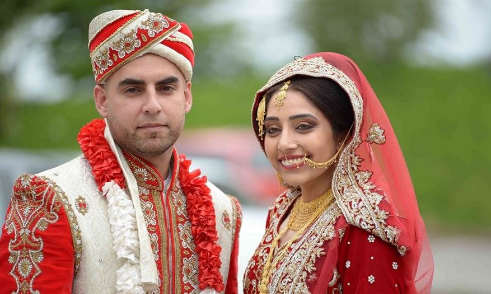 A couple sitting together at an outdoor wedding ceremony in Dubai. They appear happy and relaxed as they celebrate their love with vibrant scenery in the background. The scene captures the essence of a joyful wedding day surrounded by family and friends, showcasing decorations typical of a luxurious event in Dubai.