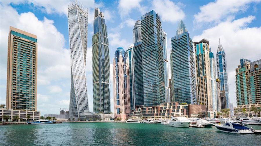 The image features Dubai's Marina with impressive skyscrapers under a partly cloudy sky. Luxury yachts float in the tranquil waters, symbolizing the vibrancy of life in this spectacular city. The iconic Cayan Tower stands out among the modern architecture, showcasing Dubai’s innovative designs while reflecting both glass and steel elements.