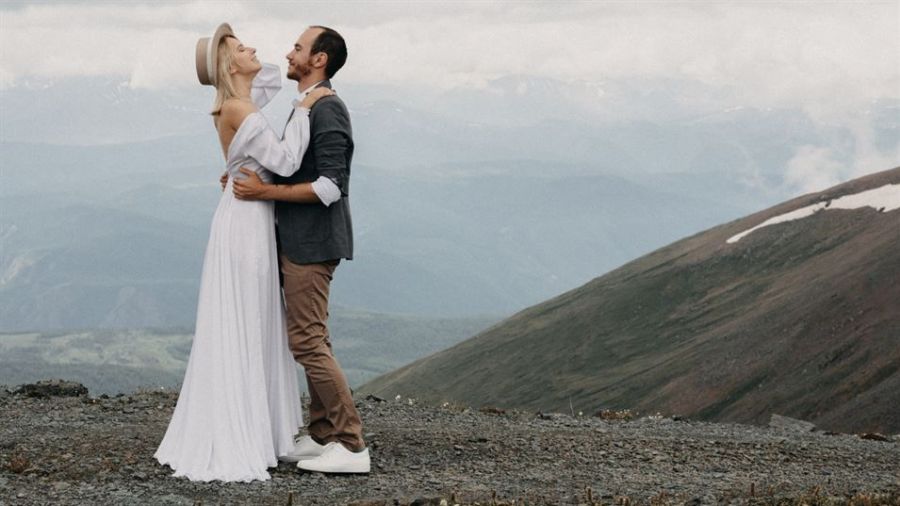 A joyful couple smiling at each other during their wedding ceremony in an elegant venue in Dubai. The background shows beautifully arranged flowers and an intimate setting perfect for celebrating love, capturing a moment filled with happiness and togetherness as they begin their life journey together.