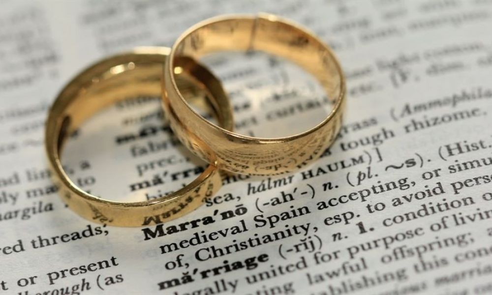 Two elegant gold wedding rings overlap on an open dictionary page showing the word “marriage.” The rings shine beautifully against a softly blurred background filled with text. This image represents commitment and love, capturing the essence of marriage in a charming way. The simple design of the rings complements their meaning, making it a delightful symbol of unity and celebration for weddings in Dubai.
