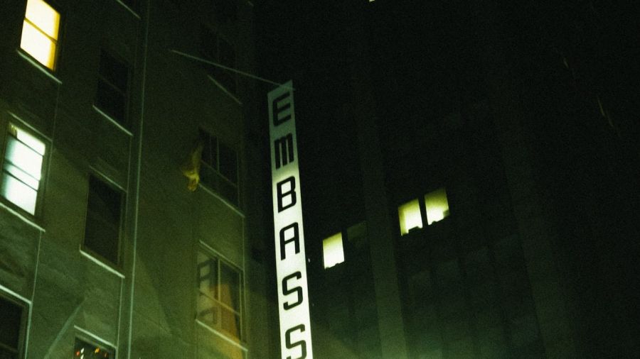 The image shows a tall building with illuminated windows labelled EMBASSY. It has a calm evening atmosphere, showcasing an urban setting where couples may seek assistance for their wedding plans in Dubai or Abu Dhabi.