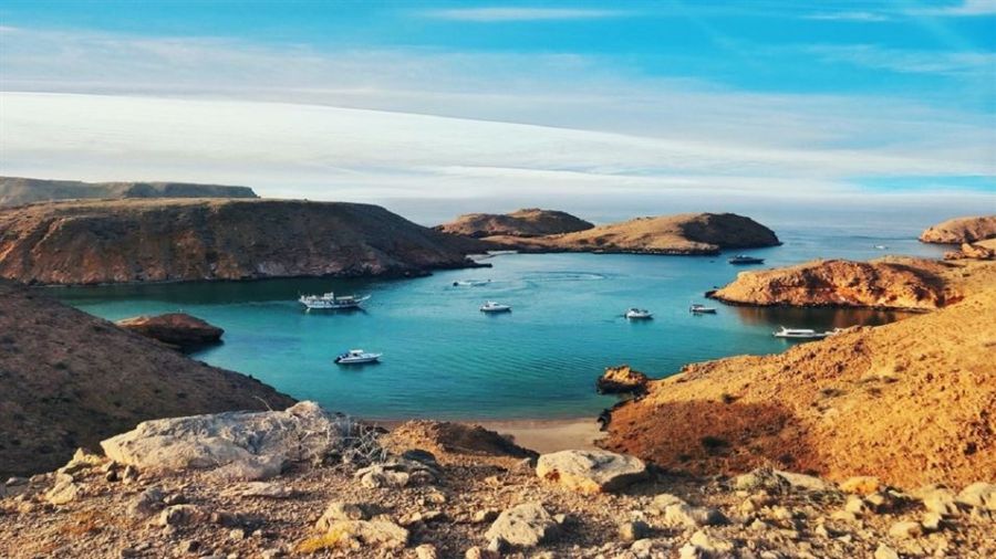 A picturesque coastal landscape shows rocky islands surrounded by calm turquoise waters. Small boats float gently in the tranquil bay while rugged terrain and scattered rocks add beauty to this serene scene. The sky above features soft clouds creating a peaceful atmosphere perfect for weddings or celebrations.