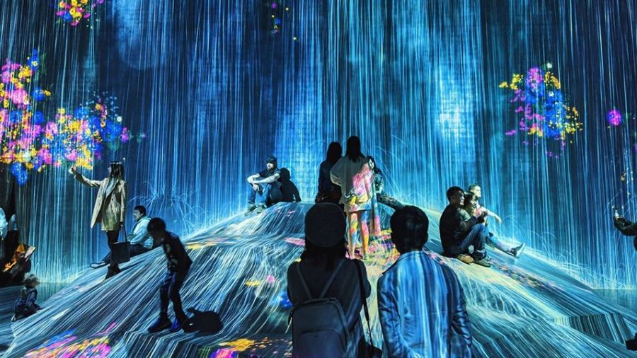 The image shows people on a vibrant digital hill surrounded by colorful lights and patterns. They are enjoying an interactive experience that combines technology and creativity in a futuristic setting.