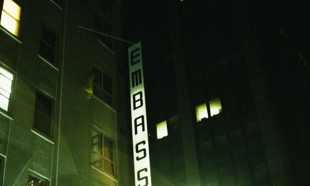 The image shows a tall building with illuminated windows labelled EMBASSY. It has a calm evening atmosphere, showcasing an urban setting where couples may seek assistance for their wedding plans in Dubai or Abu Dhabi.