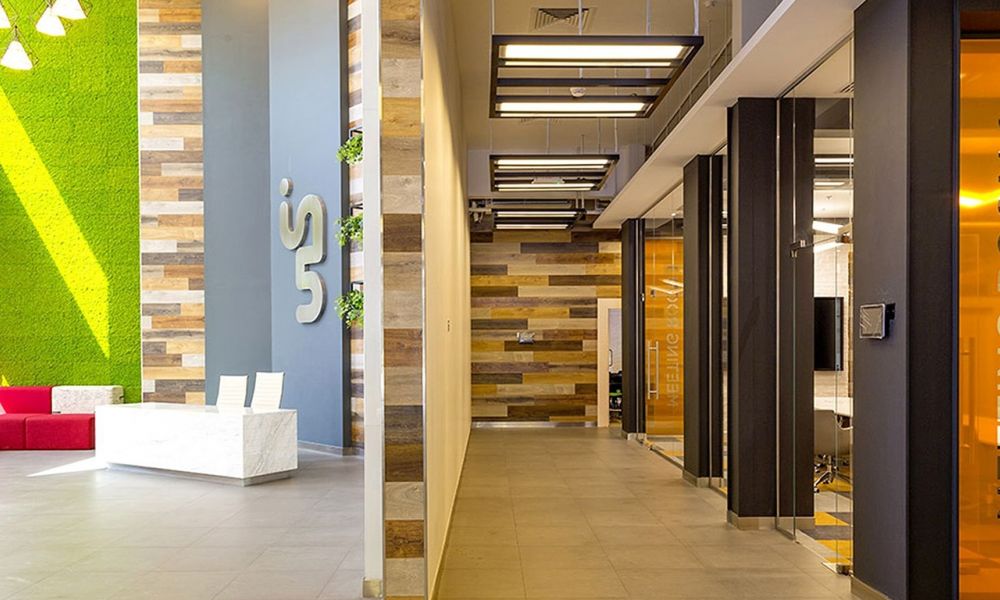 A bright office interior with a vertical garden wall, minimalist white furniture, gray tiled floor, glass-walled meeting rooms labeled Meeting Room 1, wood paneling, orange accents, and sleek lighting fixtures creating an uplifting atmosphere.