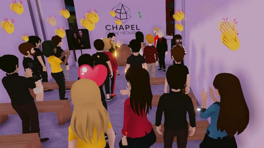 The image shows avatars celebrating a wedding ceremony inside a vibrant virtual chapel. With purple walls and wooden benches, guests are engaged at a podium where an avatar is presenting. Clapping hands and hearts float above them, demonstrating lively participation. The word CHAPEL is featured prominently on the wall, indicating this unique gathering space designed for joyous virtual celebrations like weddings.