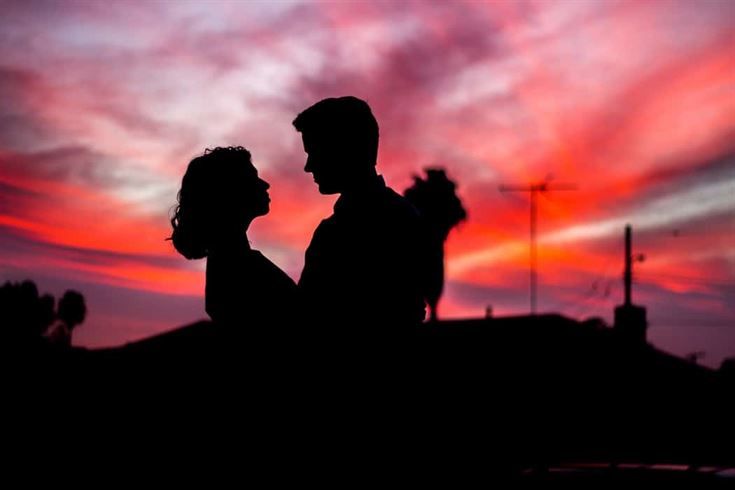 The silhouette of a loving couple embraces against a stunning sunset filled with pinks, purples, and oranges. They stand out against this beautiful backdrop while palm trees and rooftops add depth to the scene. The image captures an intimate moment filled with love and romance perfect for couples planning their weddings in Dubai or Abu Dhabi.