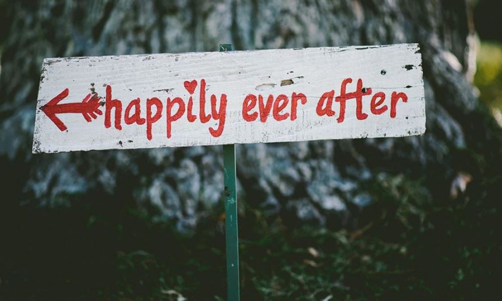 F88990D0 | What Actually Matters When You Are Planning To Get Married In The Uae Or Other Gcc Countries? | Getting Married Is A Big Decision For Any Relationship. Getting Married While Living Abroad Is A Whole New Level, Especially If Your Partner Is From Another Country Or Has A Different Religion. There Are Quite A Few Factors That Play A Role In Wedding Planning When You Live In The Uae Or Any Other Gcc Country. A rustic wooden sign that says happily ever after in red letters with an arrow pointing left. The sign is placed outdoors among greenery, suggesting a charming outdoor wedding venue. The background shows blurred trees and plants, creating a romantic atmosphere ideal for celebrating love and new beginnings.